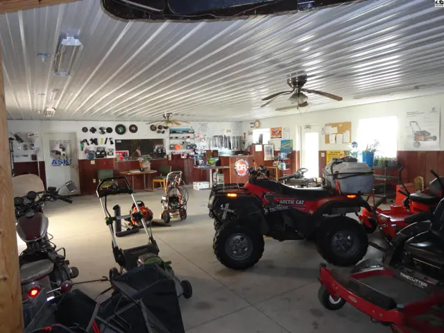 Spacious interior with white metal ceiling, concrete floor, and display of ATVs and lawn equipment.