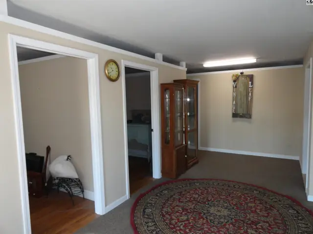 Spacious living area with neutral walls, a large circular rug, and a glass-front display cabinet.