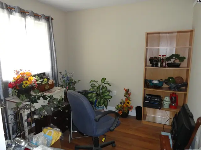 A home office with a wooden floor, light walls, a desk, chair, and a bookshelf filled with decorative items.