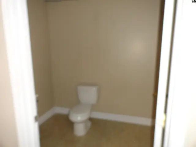 A simple toilet sits in a small, beige room with tiled flooring.