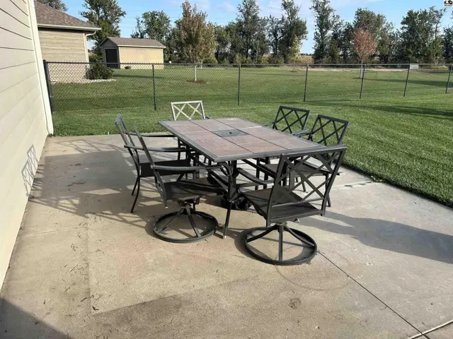 Concrete patio with a metal dining set and surrounding green lawn.