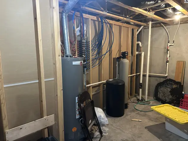 Unfinished basement with water heater, water softener, and exposed framing.