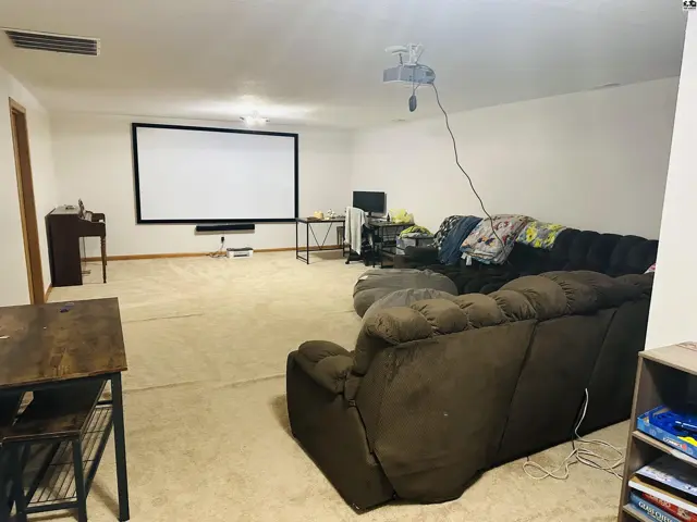 Spacious room with a large projection screen, comfortable seating, and carpeted flooring.