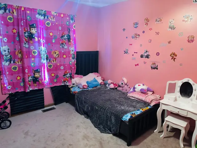 This room features pink walls, a bed, and a vanity with a stool.