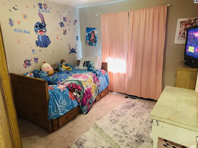 Carpeted bedroom with a wooden bed frame, pink curtains, and wall decor.
