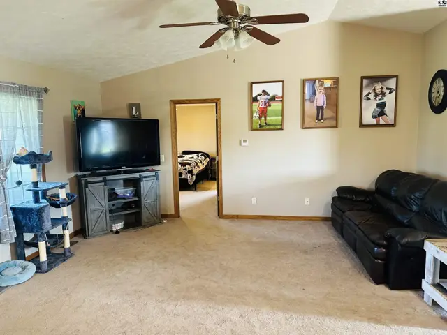 Spacious living room with vaulted ceiling, carpet, and a view into another room.