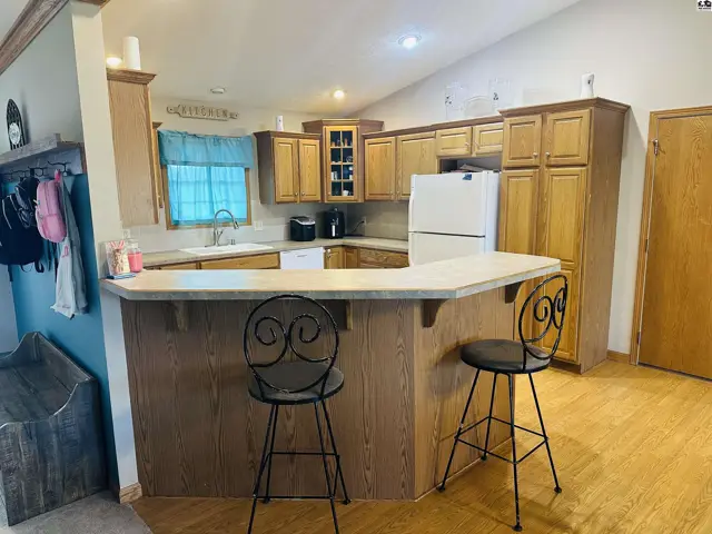 This kitchen features light wood cabinetry, a breakfast bar, and a white refrigerator.