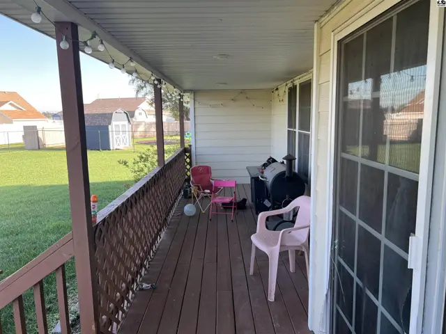 Covered wooden porch with railing, outdoor furniture, and string lights.