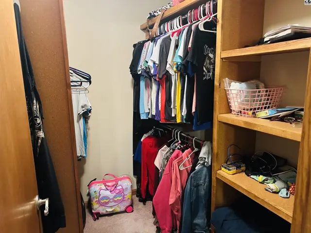 Walk-in closet with wood shelving, hanging rods, and carpeted floor.