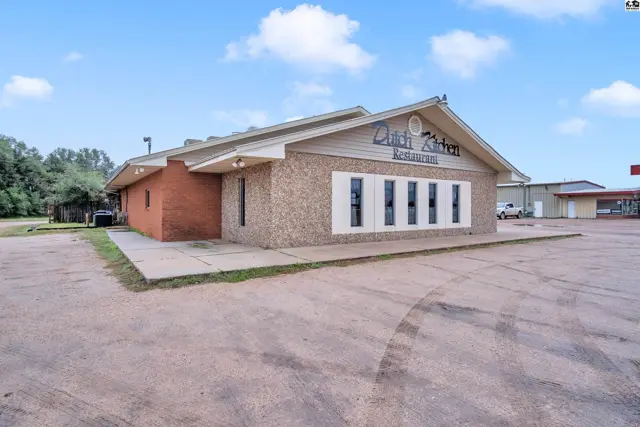 Commercial building exterior with brick and textured siding, featuring a prominent sign and multiple windows.