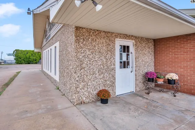 Commercial building exterior with textured facade, brick accents, and a white door with decorative planters.