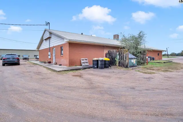 Brick building with a gravel lot, featuring industrial barrels and a dumpster near the rear entrance.
