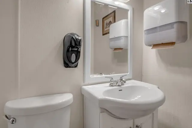 A clean bathroom with a white vanity, sink, toilet, and wall-mounted dispensers.