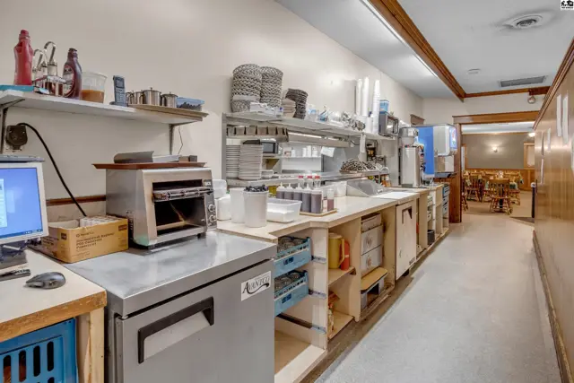 Commercial kitchen with stainless steel appliances, ample shelving, and a computer workstation.