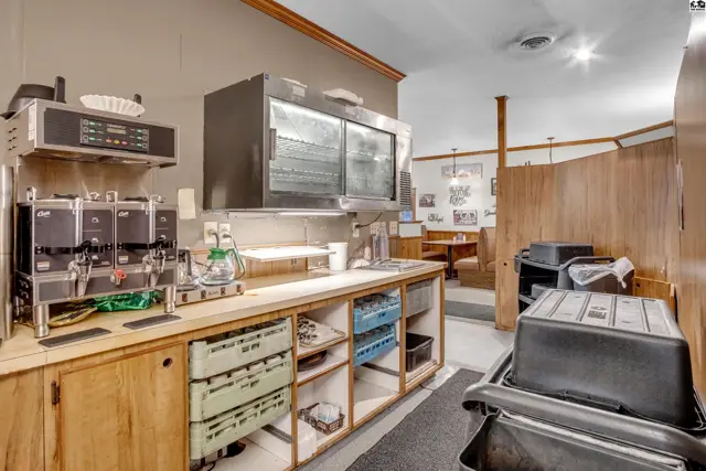 Commercial kitchen area with stainless steel appliances, wooden cabinetry, and dining booths visible in background.