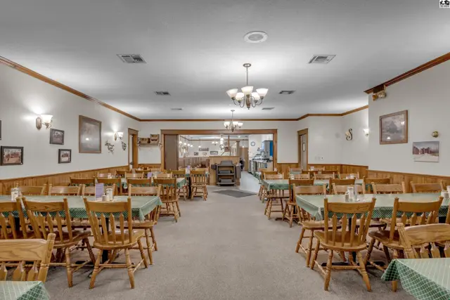 Spacious dining room with wood-paneled walls, green-covered tables, and wooden chairs.
