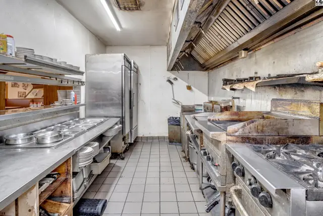 Commercial kitchen with stainless steel appliances, tiled floors, and a large exhaust hood.