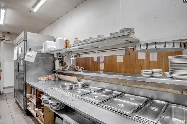 Commercial kitchen with stainless steel counters, warming trays, and ample shelving stocked with dishes.