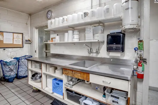Commercial kitchen prep area with stainless steel counters, sink, shelving, and storage.
