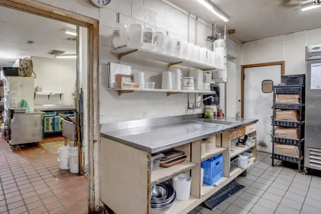 Commercial kitchen with stainless steel counters, tiled floors, and ample shelving.