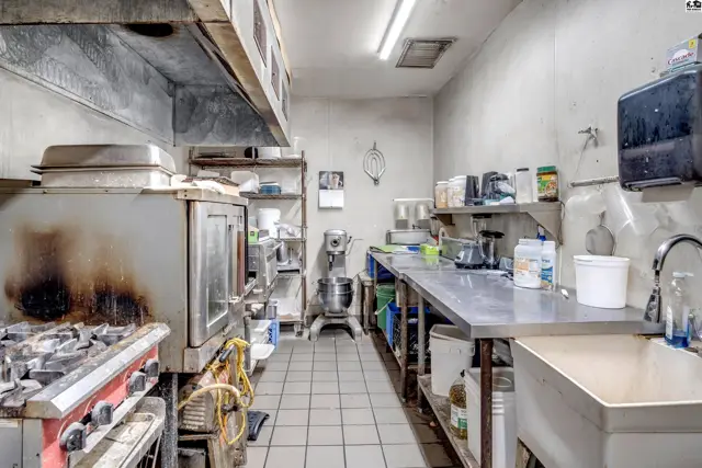 Commercial kitchen with stainless steel counters, commercial oven, stove, mixer, and tiled floor.
