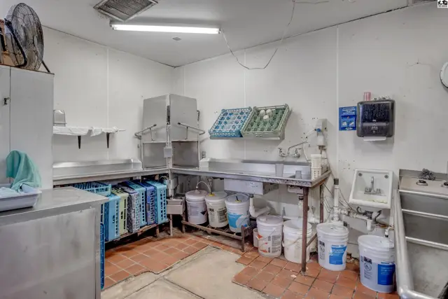 Commercial kitchen prep area with stainless steel counters, industrial sink, and storage racks.