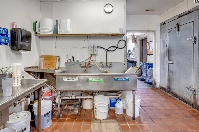 Commercial kitchen with stainless steel sink, tiled floor, and walk-in cooler.