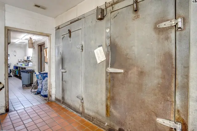 Commercial walk-in refrigerators with metal doors and tiled flooring lead to a prep area.