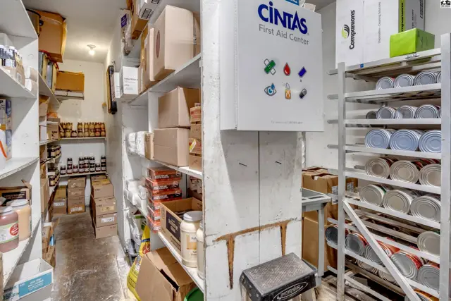 Storage room with shelves stocked with boxes, jars, and canned goods, featuring a Cintas First Aid sign.