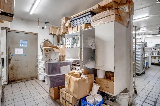 Commercial kitchen storage area with tiled floors, metal shelving, and stacked boxes.