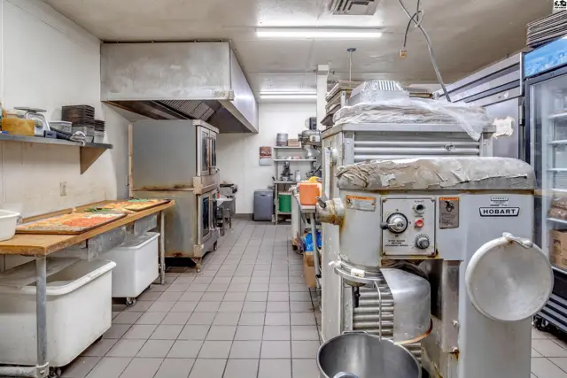 Commercial kitchen with stainless steel appliances, ovens, mixers, and tiled floors.