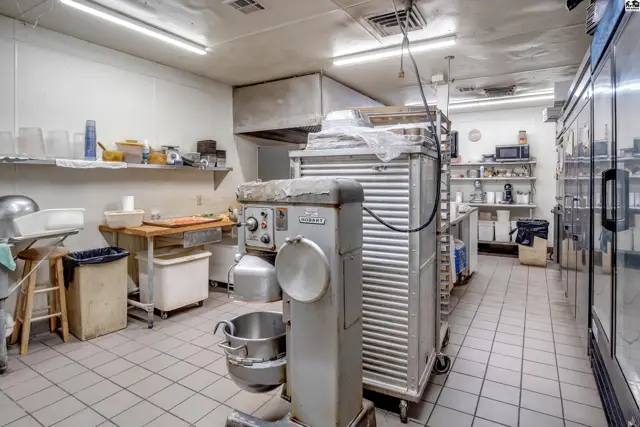 Commercial kitchen with stainless steel appliances, tiled floors, and ample shelving.