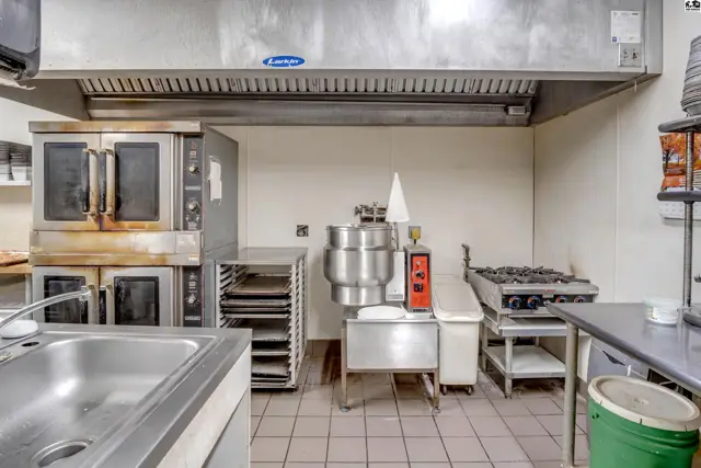 Commercial kitchen with stainless steel appliances, ovens, a gas range, and a large sink.