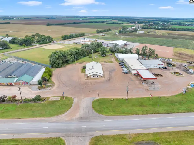 Aerial view of commercial buildings, including a gas station and greenhouse, surrounded by fields.