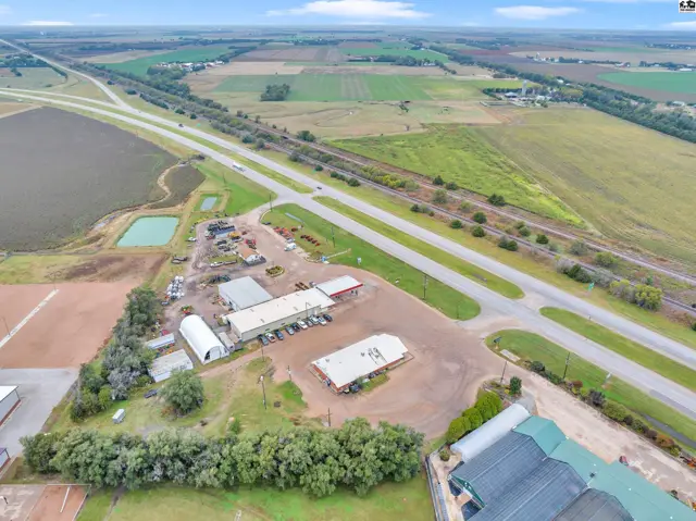 Aerial view of commercial buildings and agricultural fields adjacent to a highway and railroad tracks.