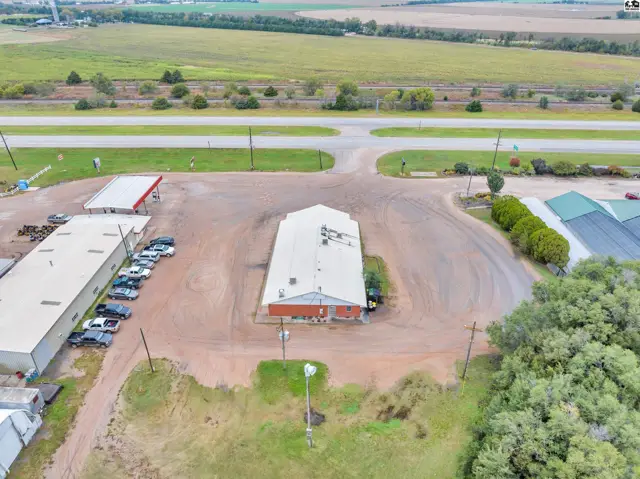 Aerial view of a commercial building with a large parking lot, adjacent to a highway and fields.