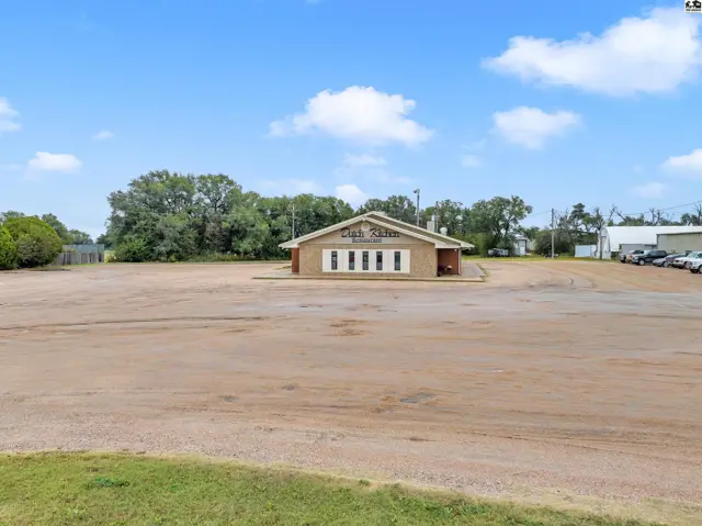 Brick building with large windows and a paved lot under a bright blue sky.