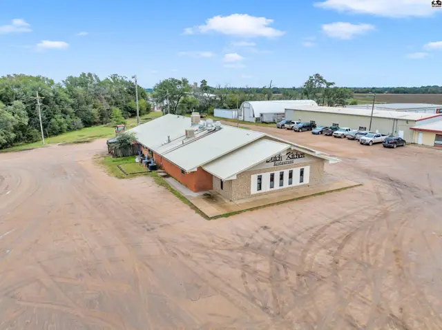 Commercial building with brick facade and metal roof, surrounded by gravel lot and parking.