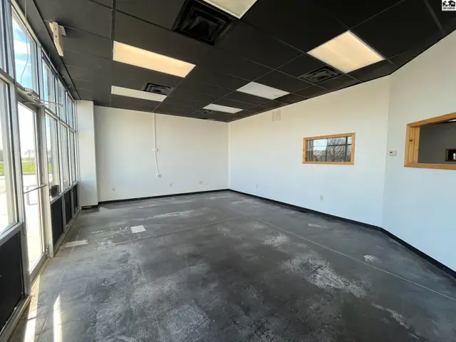 Spacious commercial interior with large windows, concrete floors, and a black drop ceiling.