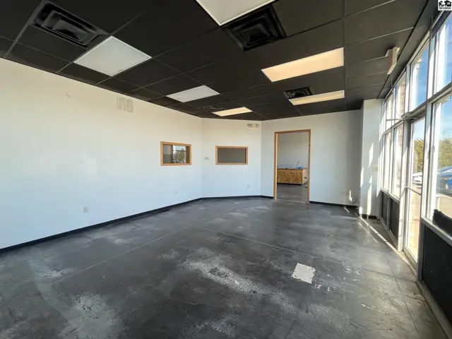 Empty commercial space with white walls, dark flooring, and large windows.