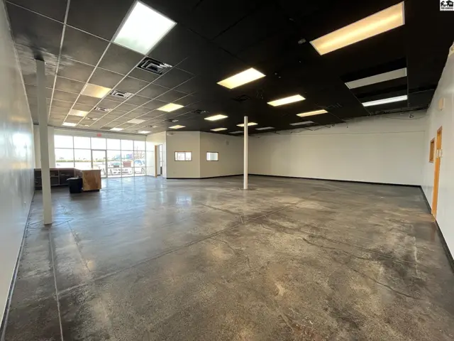 Spacious commercial interior with polished concrete floors, large windows, and a black drop ceiling.