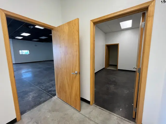 Two open wooden doors reveal a modern commercial space with polished concrete floors and bright lighting.