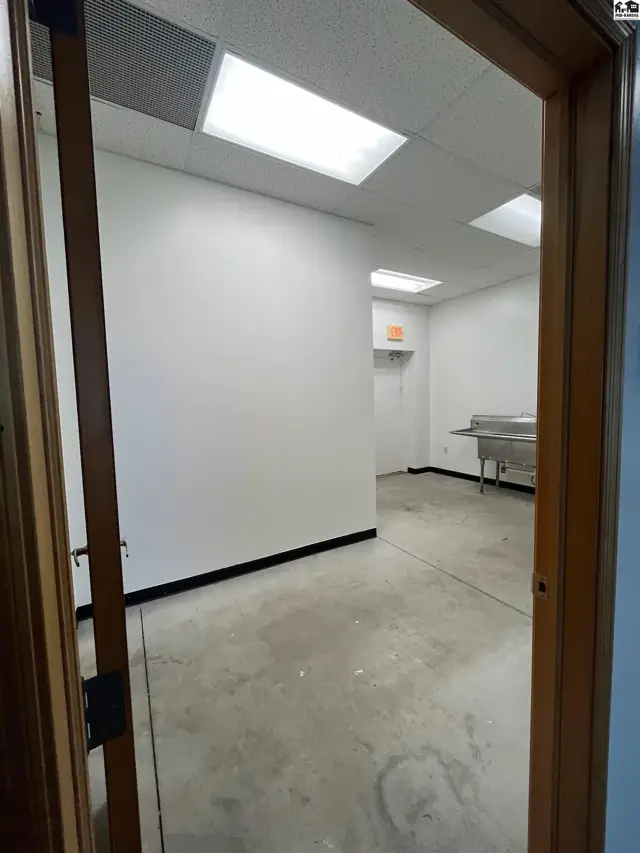 Empty commercial space with white walls, concrete floors, and a stainless steel sink.