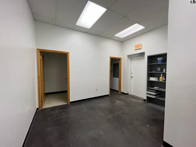 Empty office space with white walls, dark flooring, and wooden doors.