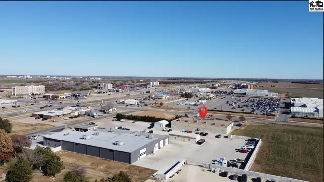 Aerial view of a commercial building with a large parking lot and surrounding businesses under a clear blue sky.