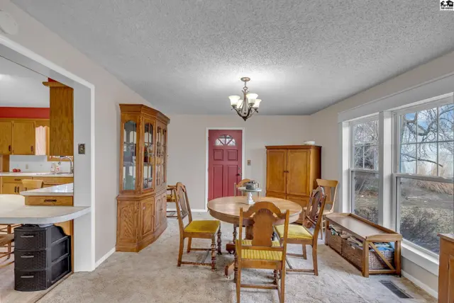 Dining room with a round wooden table, chairs, china cabinet, and large windows.