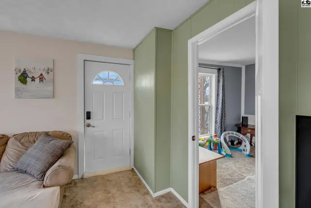Living room with beige sofa and white door, opening to a room with children's toys.
