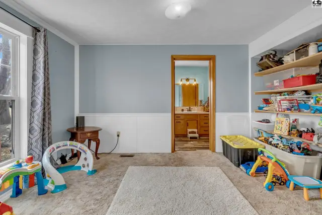 Light blue and white paneled room with a doorway to a bathroom, and toys scattered on the carpet.