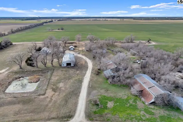 Aerial view of a rural property with barns, a pond, and surrounding farmland under a blue sky.