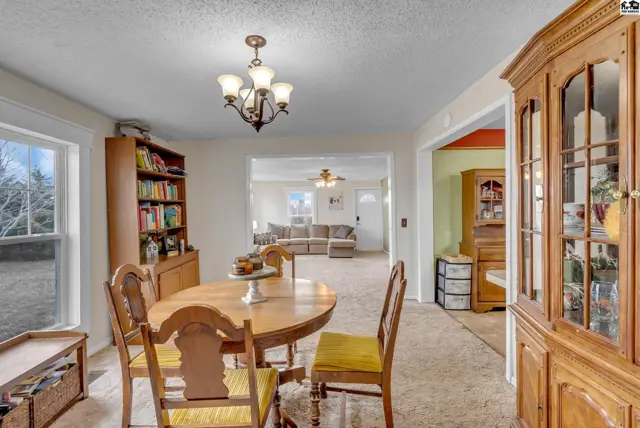 Warm dining room with a wooden table, chairs, and a large hutch, opening to a living area.